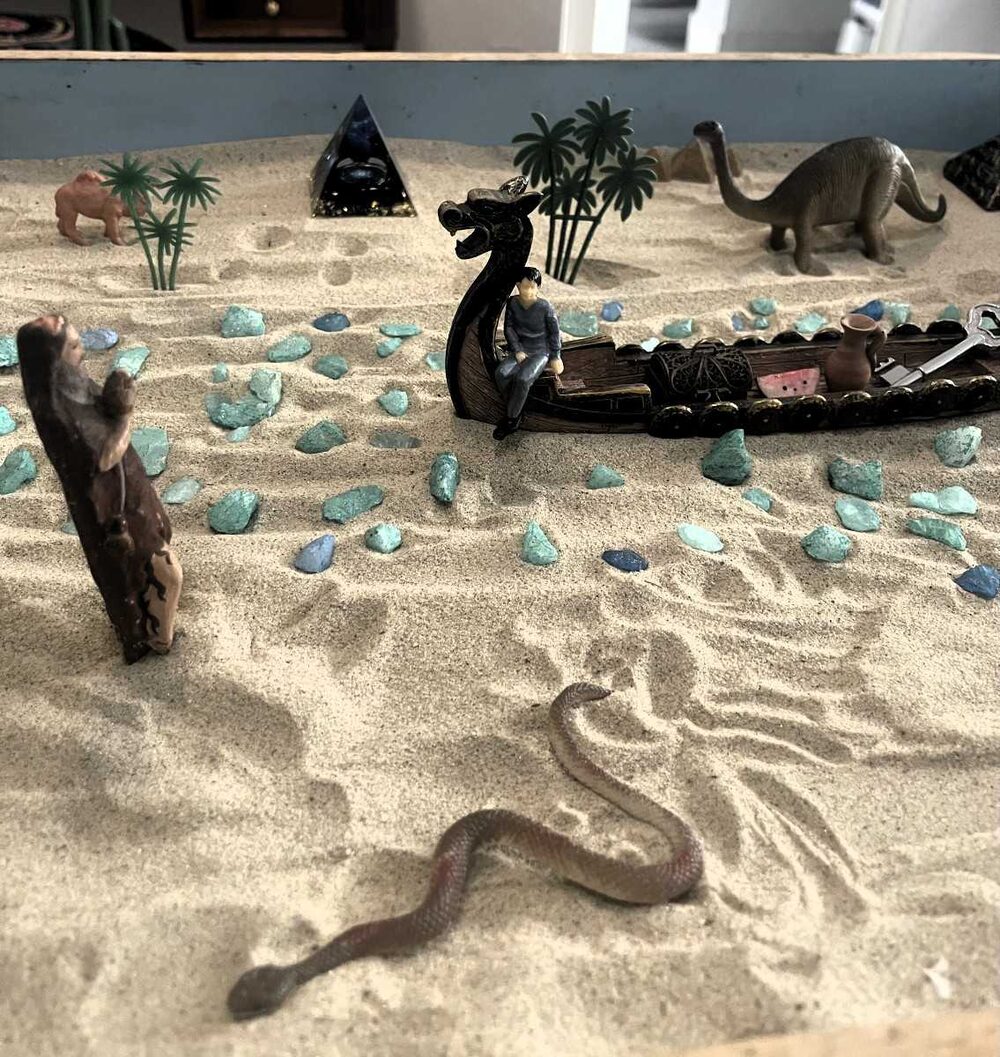 Caixa de areia do consultório com miniaturas, pedras e um barco